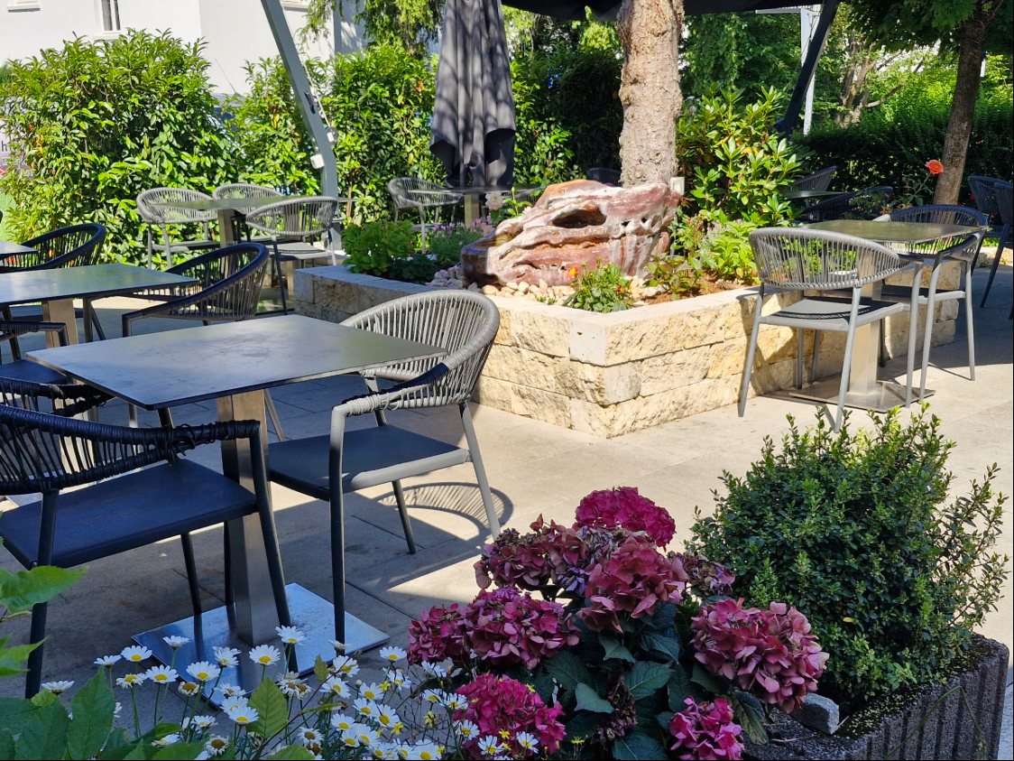 Gartenterrasse mit Tischen, Blumen und Brunnenstein